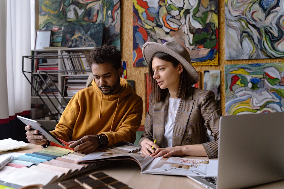 Two designers collaborate in an art-filled studio, engaging with design materials and digital devices.